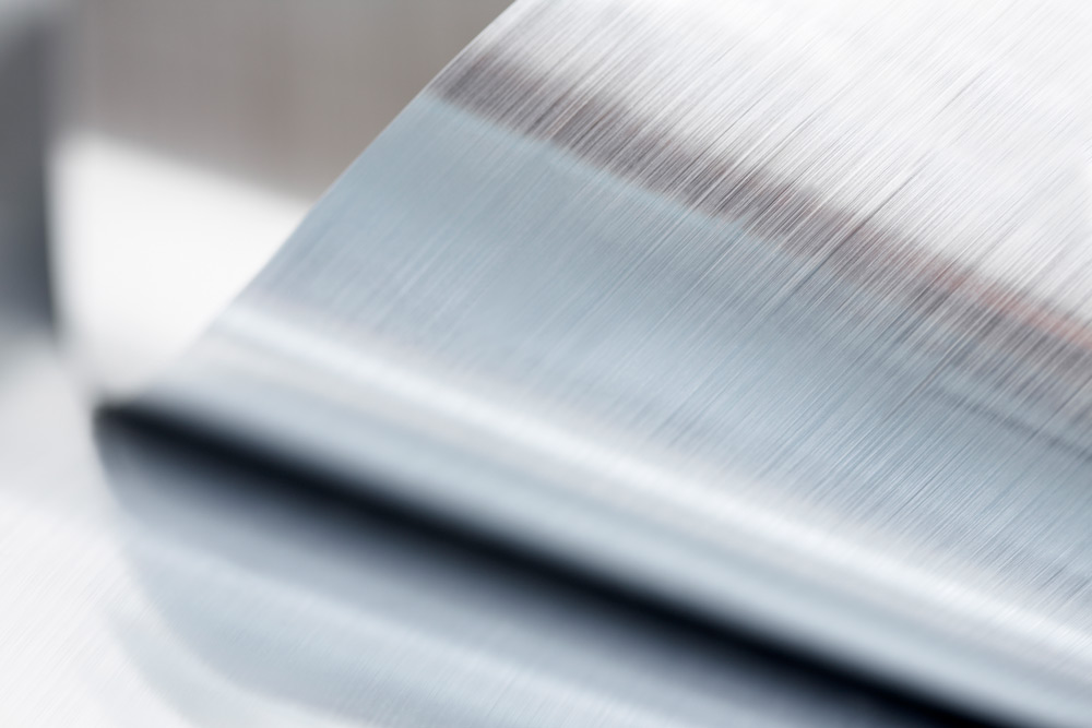 Bilden visar ett närbild av ett oprullat metallark med en borstad och silverfärgad yta i aluminium.